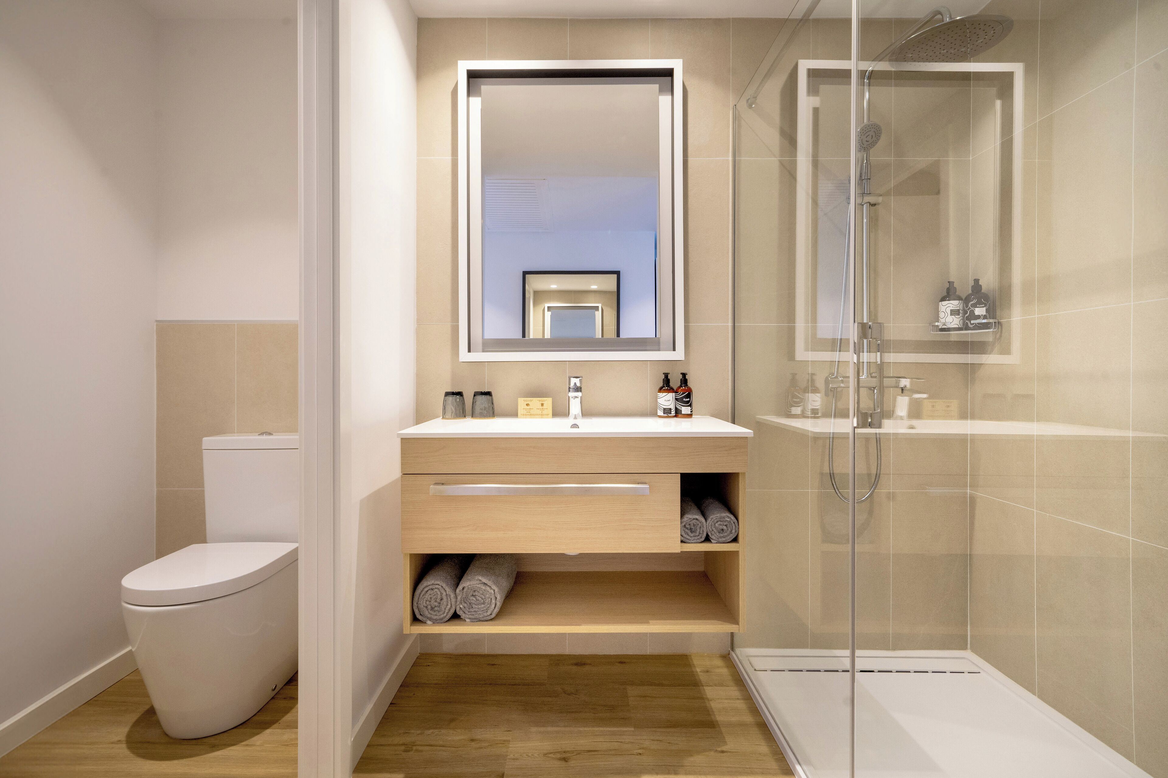 A modern bathroom with a toilet, vanity with a mirror, and a glass-enclosed shower.