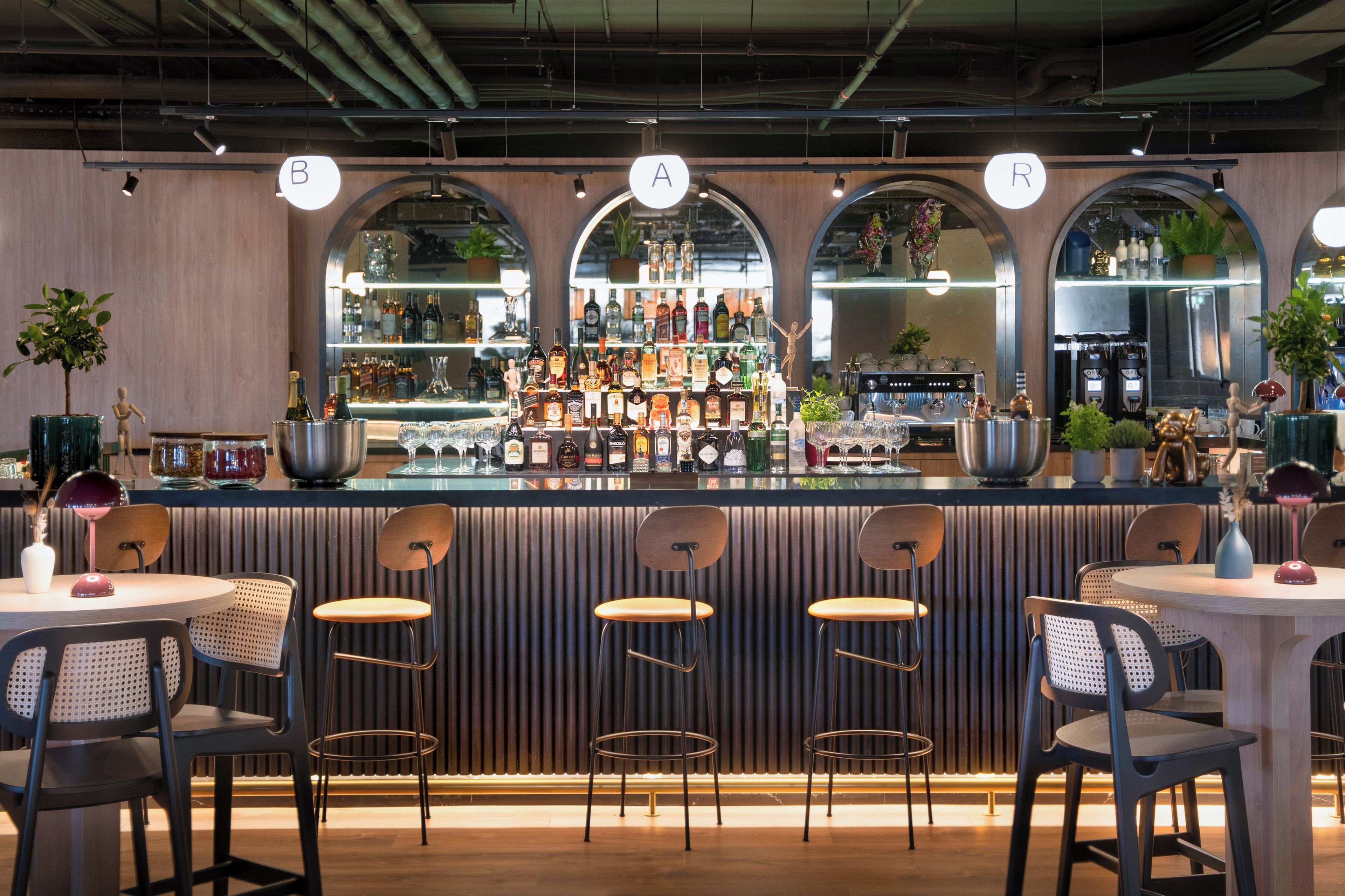 Eine Bar mit einer Theke, auf der verschiedene Flaschen und Gläser stehen, umgeben von Sitzgelegenheiten.