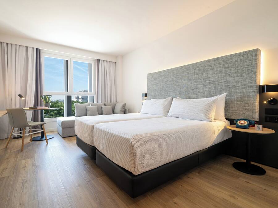 Een moderne hotelkamer met twee bedden, een bureau en uitzicht op de stad.