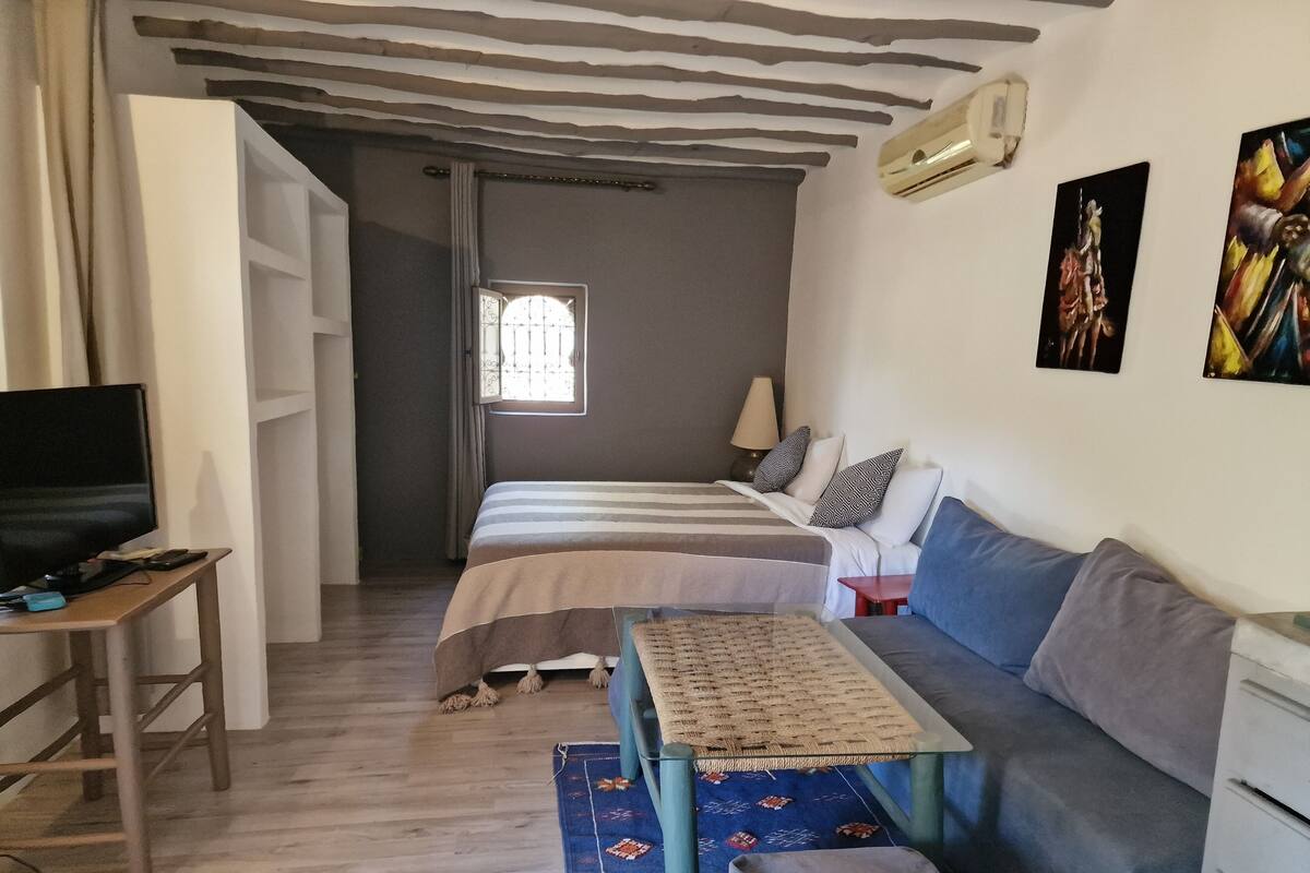 A bedroom with a bed, a sofa, a TV, and a small table.