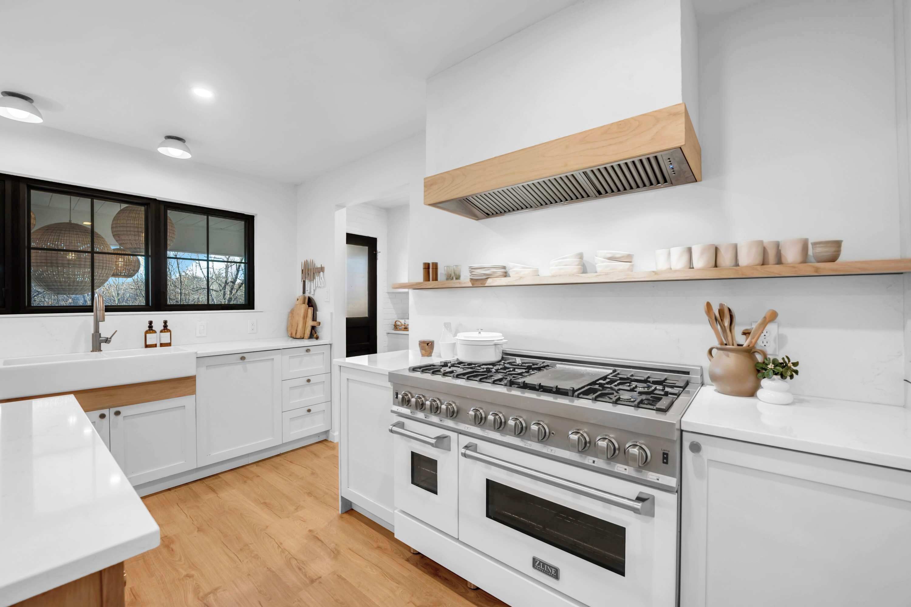 A modern kitchen with white cabinetry, a stainless steel stove, and a wooden ceiling vent.