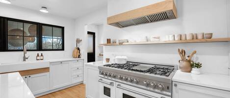 A modern kitchen with white cabinetry, a stainless steel stove, and a wooden ceiling vent.