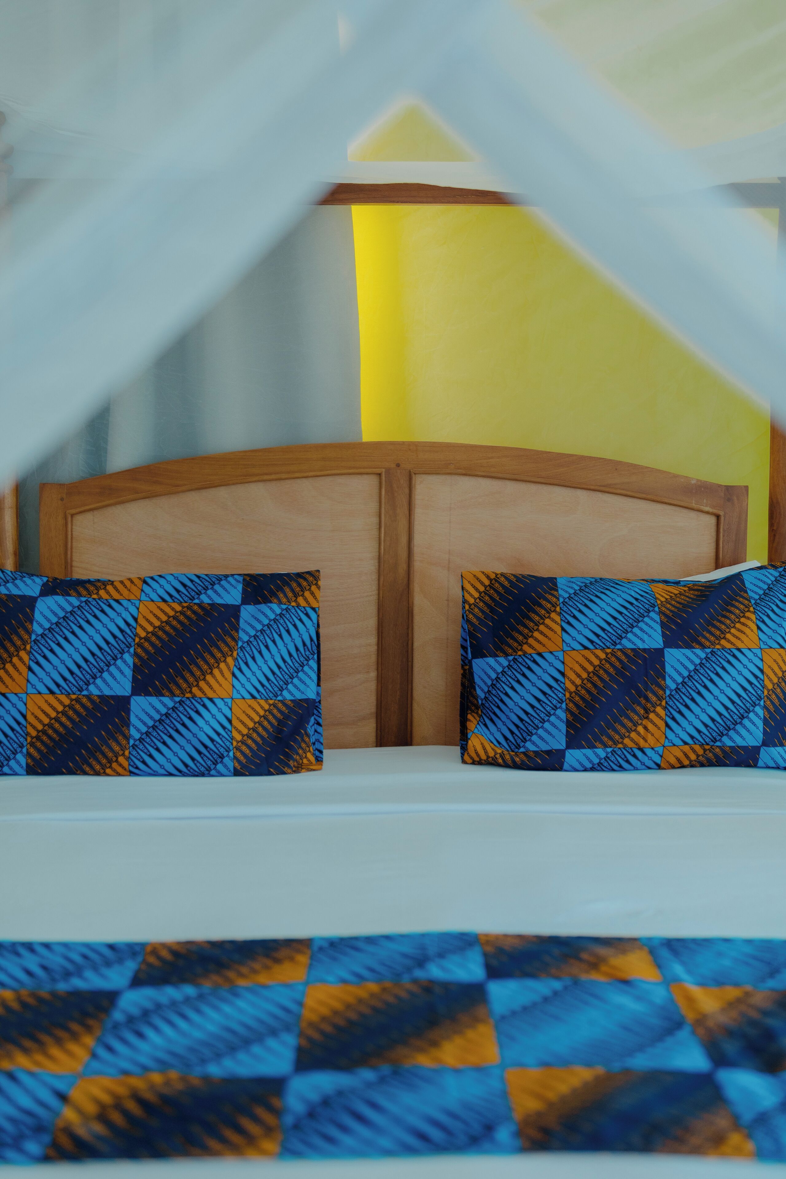 Una cama con cabecera de madera y dos almohadas con estampado a cuadros.