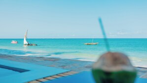 A poolside view with a coconut drink, boats on the water, and a clear sky.
