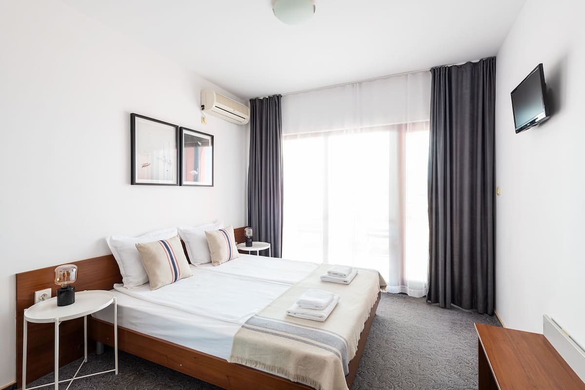 A hotel room with a bed, bedside table, lamp, and a TV on the wall.