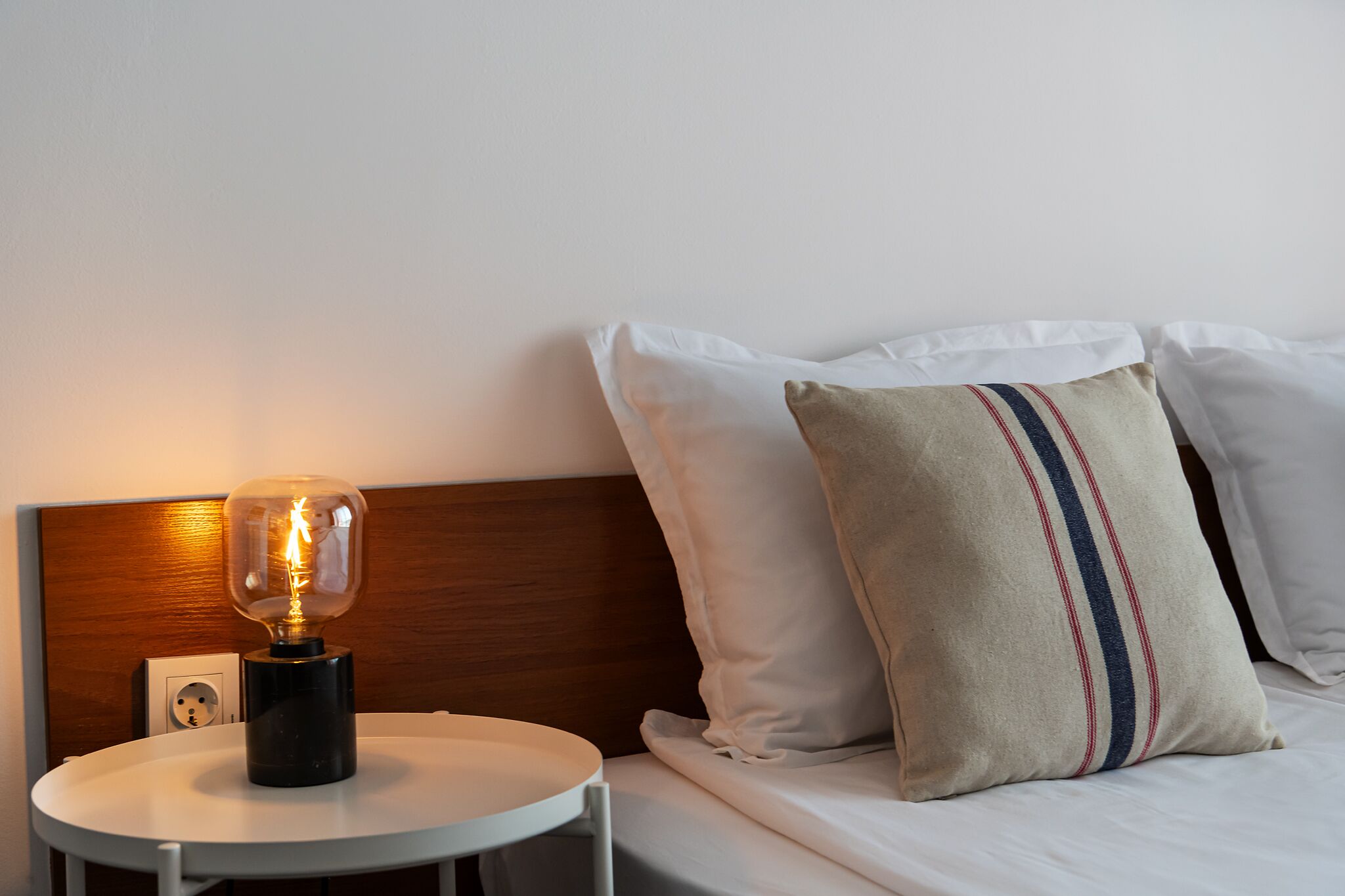 A neatly made bed with white linens and a pillow with a striped pattern.