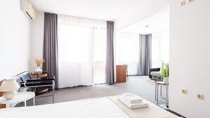 A hotel room with a bed, a desk, a chair, a small table with a plant, and a window with curtains. - Afrodita 2 (Nessebar)