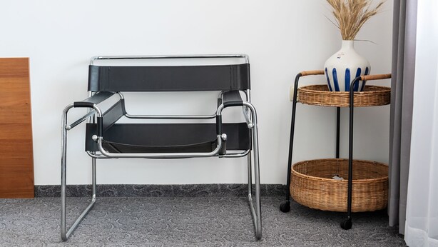 Une chaise en métal noir avec une structure en chrome, un panier en osier posé sur un support métallique et un vase blanc contenant des plantes séchées.