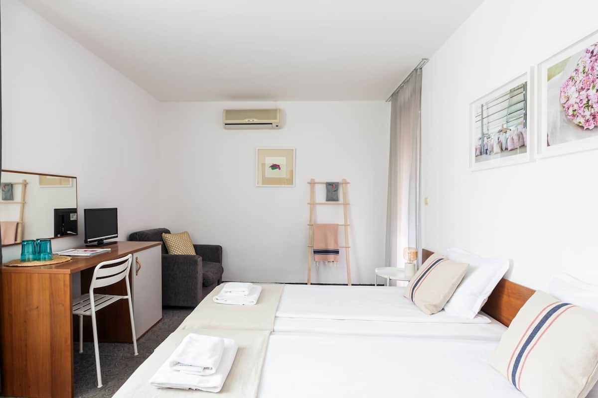 A hotel room with a bed, a desk, a chair, a TV, and a small table.