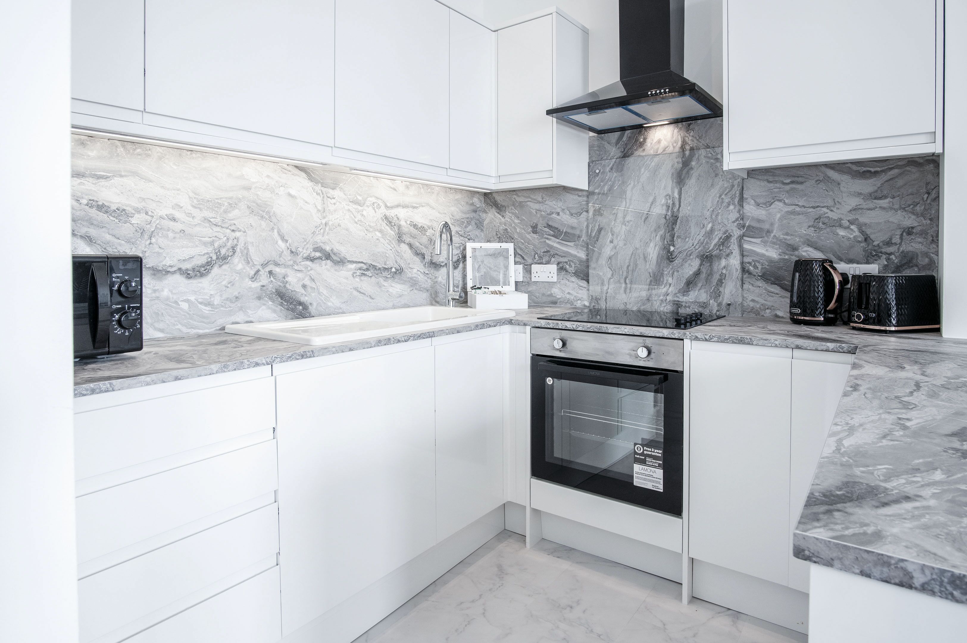 A modern kitchen with white cabinetry, a marble backsplash, a black oven, and a coffee machine.