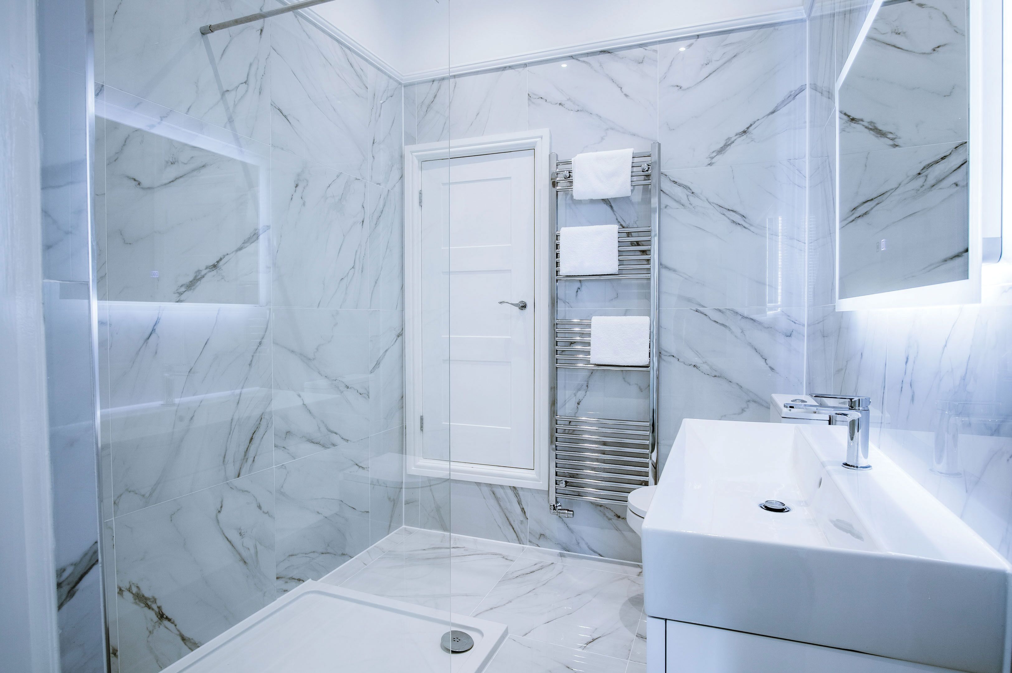 A modern bathroom with a glass shower enclosure, a white sink, and a marble-tiled shower area.