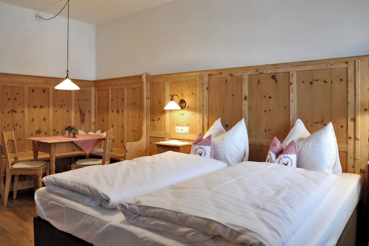 A room with two beds, a wooden headboard, a table with a checkered tablecloth, and a chair.