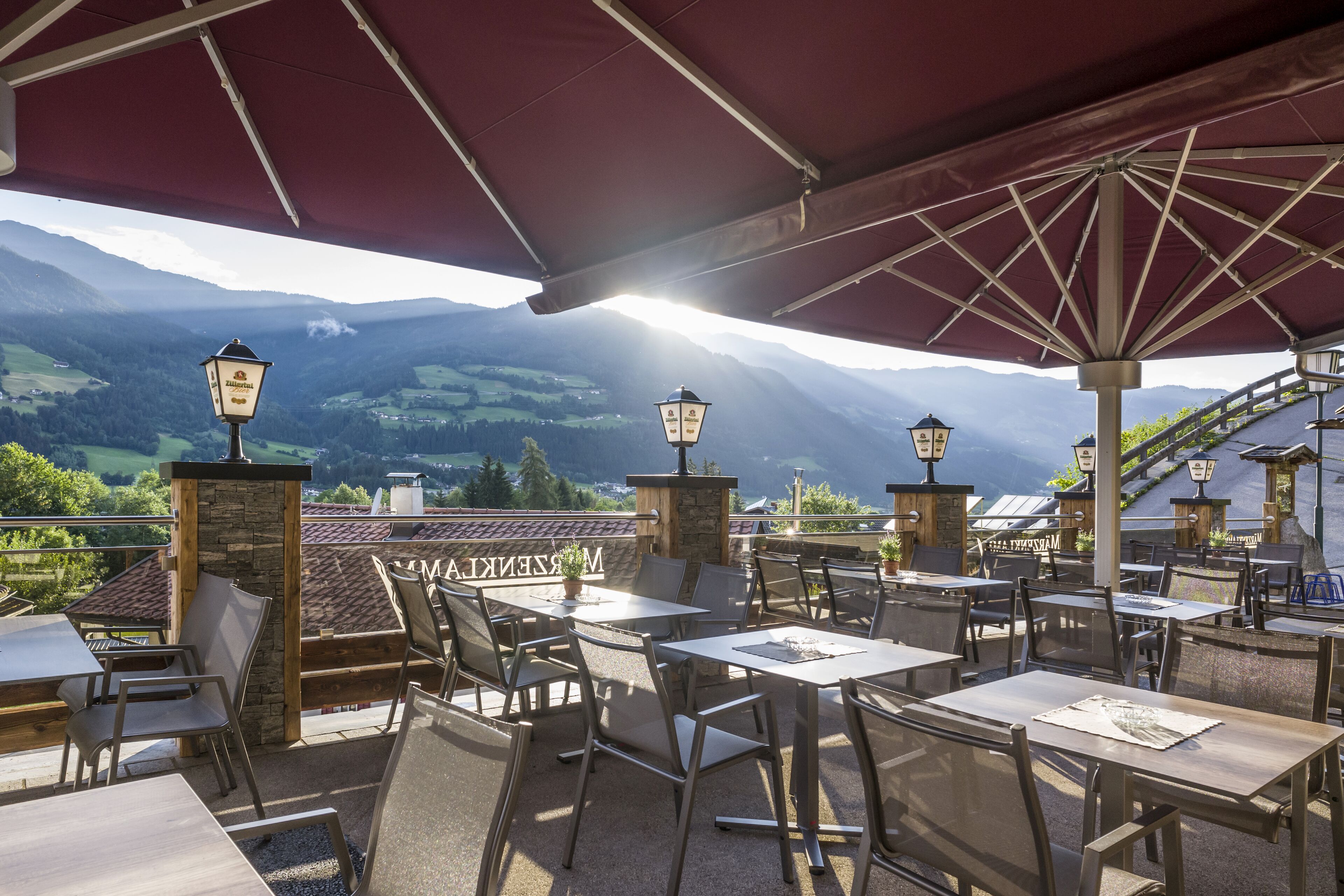 An outdoor patio with tables and chairs, stone pillars, and hanging lanterns.