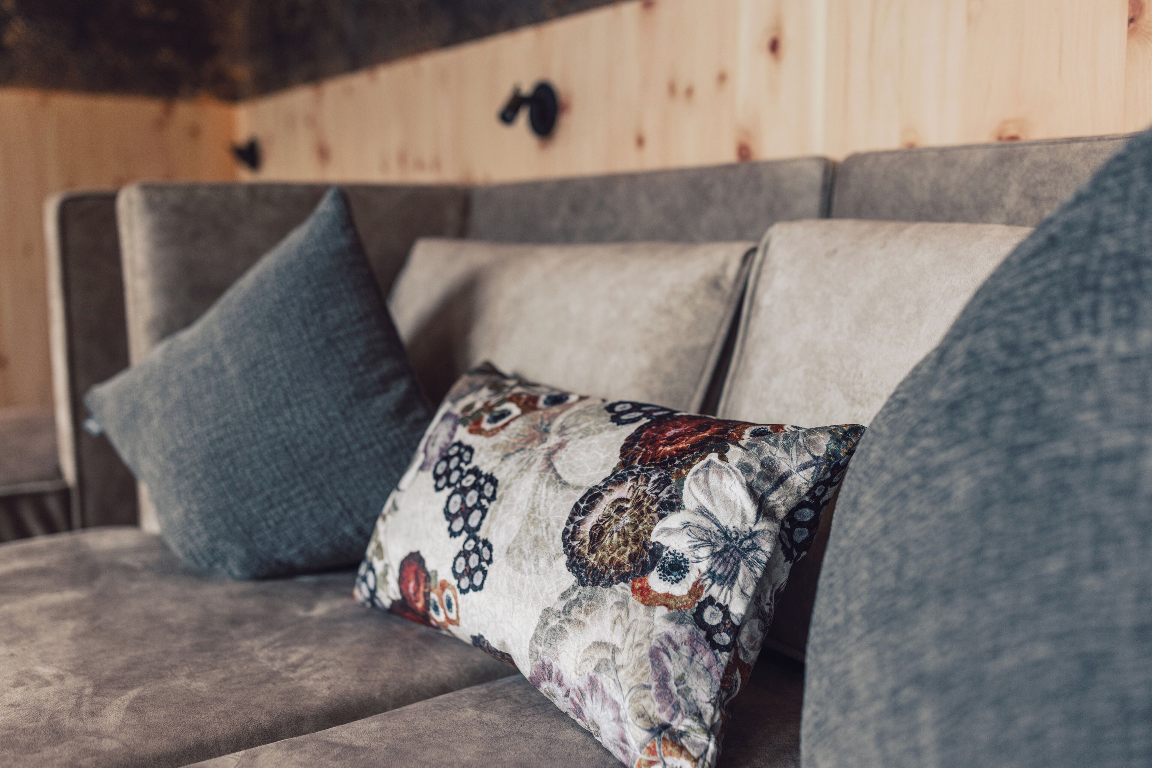 Ein graues Sofa mit drei Kissen, eines schlicht blau und zwei mit Blumenmustern.