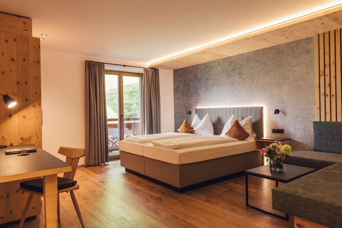 A modern hotel room with a large bed, a dining table, and a sofa.