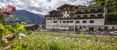 A hotel with multiple balconies, a mountain view, and a garden in the foreground.