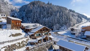 A snow-covered village with wooden buildings, a stone wall, and a mountain in the background. - Hotel Märzenklamm Stumm im Zillertal (Stumm)