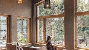 A room with large windows, a wooden bench, and a hanging light fixture. - Hotel Märzenklamm Stumm im Zillertal (Stumm)