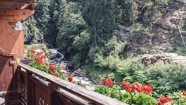 A wooden balcony with a view of a river and forested mountains. - Hotel Märzenklamm Stumm im Zillertal (Stumm)