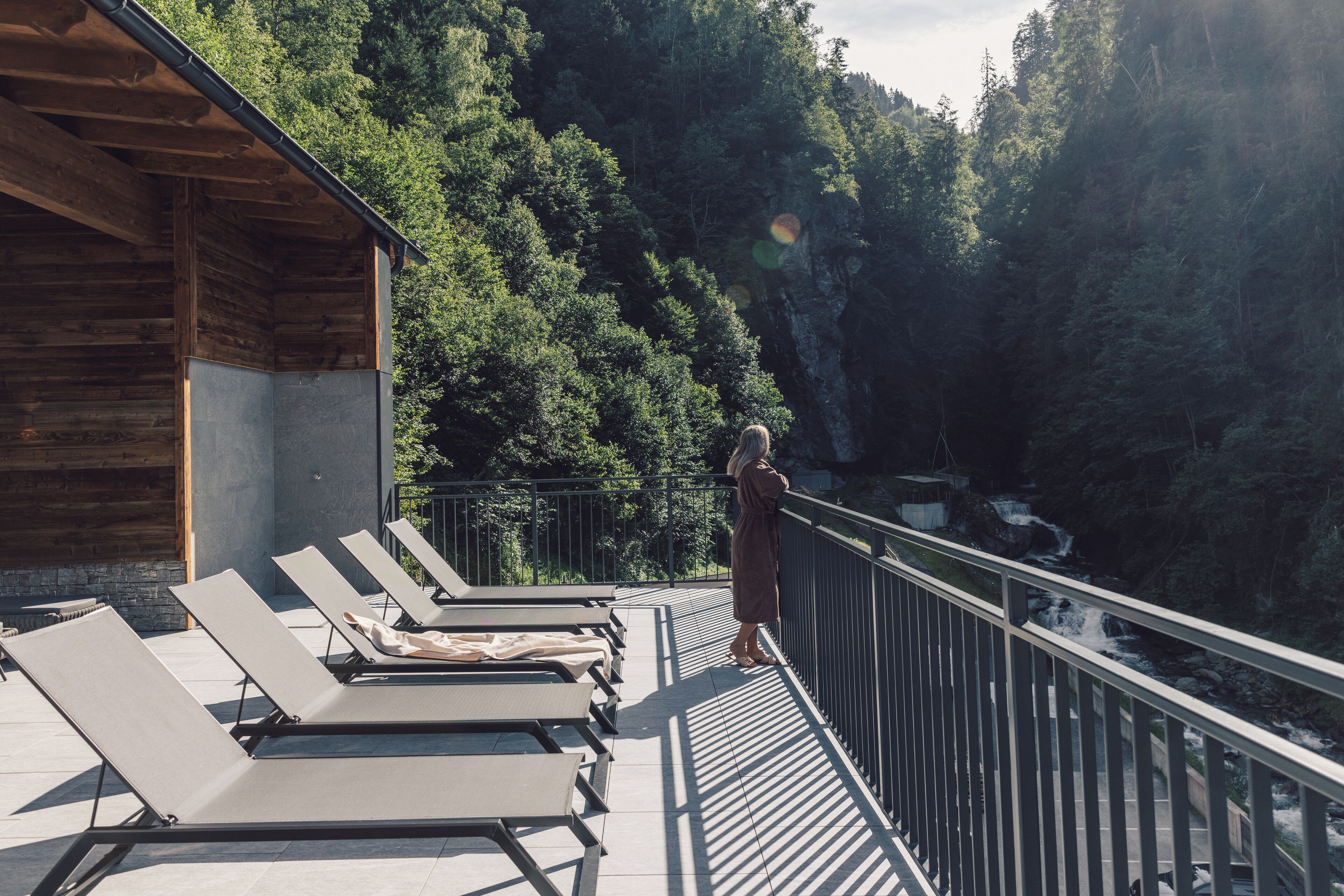 A balcony with sun loungers overlooking a forested area and a waterfall.