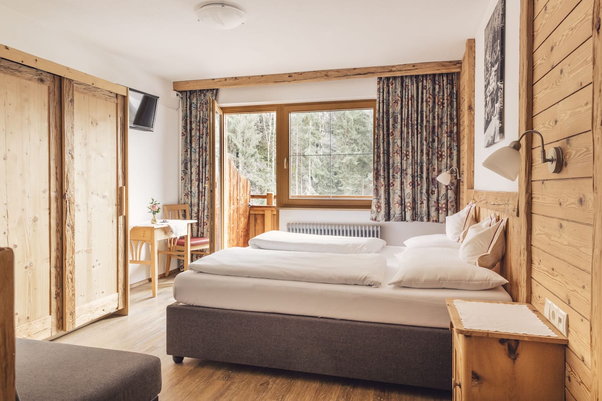 A bedroom with a large bed, wooden walls, a window with curtains, a desk, and a chair.