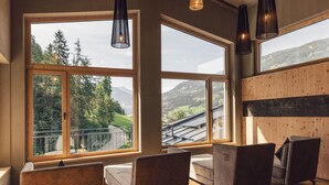 A room with large windows offering a view of mountains and greenery. There are cushioned seating areas and pendant lights. - Hotel Märzenklamm Stumm im Zillertal (Stumm)