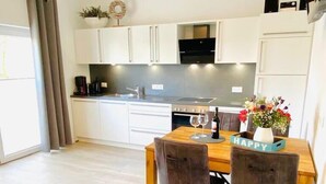 A modern kitchen with white cabinets, a dining table with two chairs, and a small rug on the floor.
