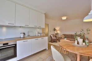 A modern kitchen with white cabinets, a built-in oven, and a dining area with a wooden table and chairs.