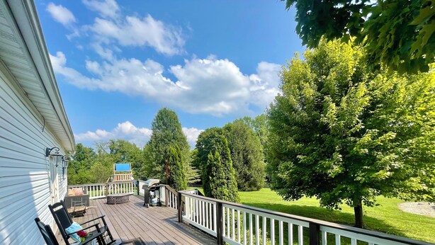 Une terrasse en bois avec des meubles d’extérieur, un barbecue et une vue sur une pelouse verdoyante et des arbres.