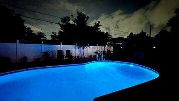 A swimming pool with a curved edge, surrounded by a white fence and palm trees.