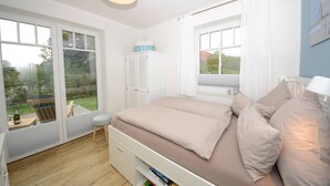 Quarto com cama, janela, cadeira e mesa pequena.