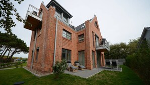 Uma casa moderna de tijolo com telhado plano, varanda e área de pátio com mobiliário de exterior.