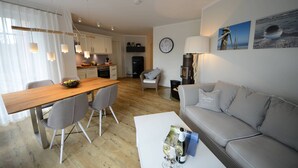 Uma sala de estar moderna com uma mesa de jantar de madeira, cadeiras cinzas, um sofá cinza e uma mesa de centro com copos de vinho e uma revista.