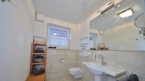 Une salle de bain moderne équipée de toilettes, d’un lavabo et d’une étagère en bois où sont rangées des serviettes.