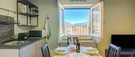 A dining area with a table set for four, a kitchen with a microwave, and a view of mountains through a window.