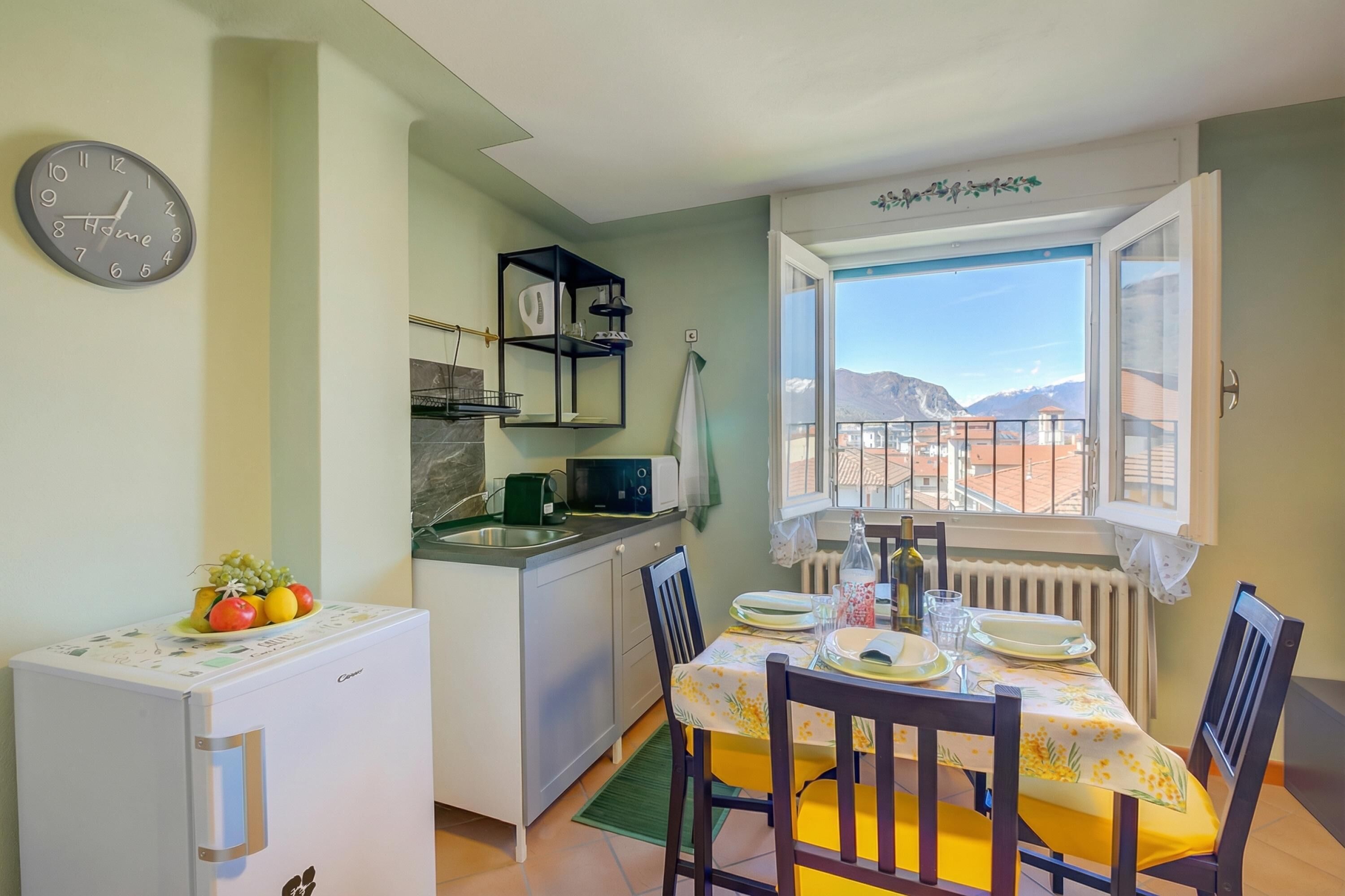 A compact kitchen with a dining area, a clock, and a view of mountains through a window.