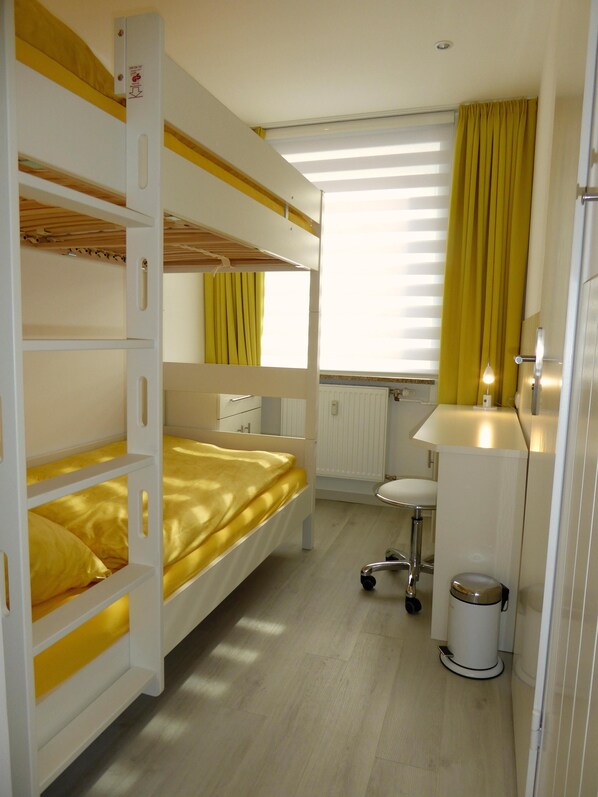 A bunk bed room with a desk and a small bathroom.