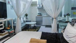 A hotel room with a bed, a TV, a small table, and a kitchenette. - Azure 1BR Citylights With Netlfix Near Airport (Parañaque)