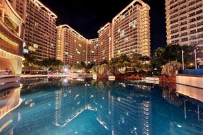 Vista nocturna de un hotel con varios edificios altos, una piscina central y vegetación circundante.