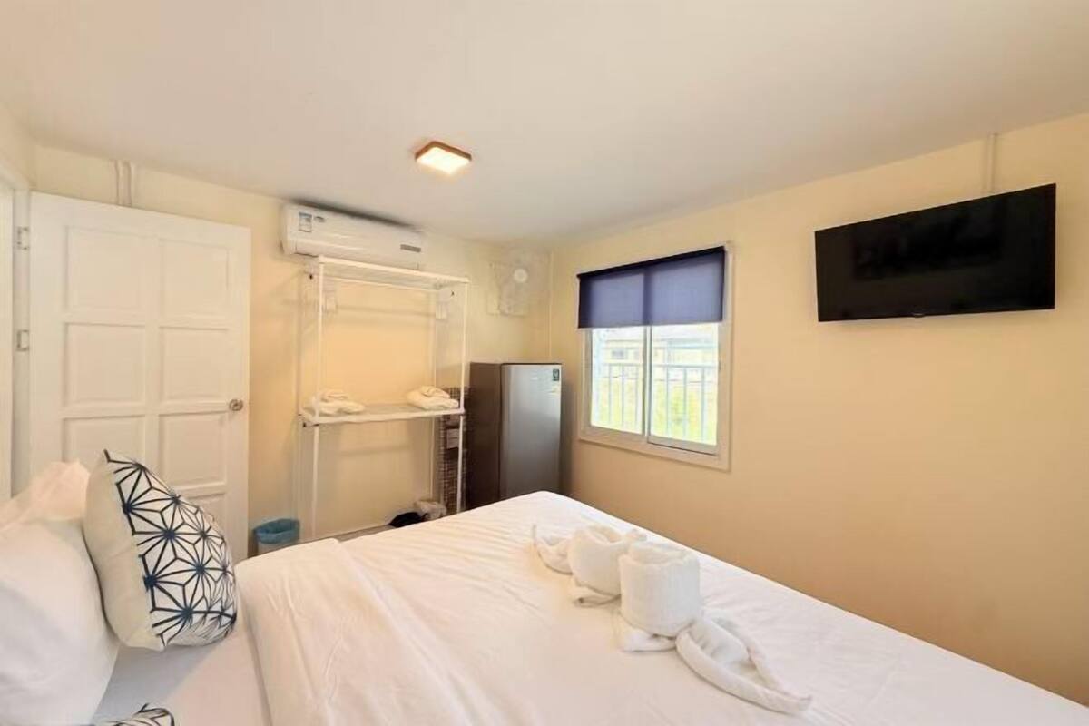 A hotel room with a bed, a TV, a window with a view, a wardrobe, and an air conditioning unit.