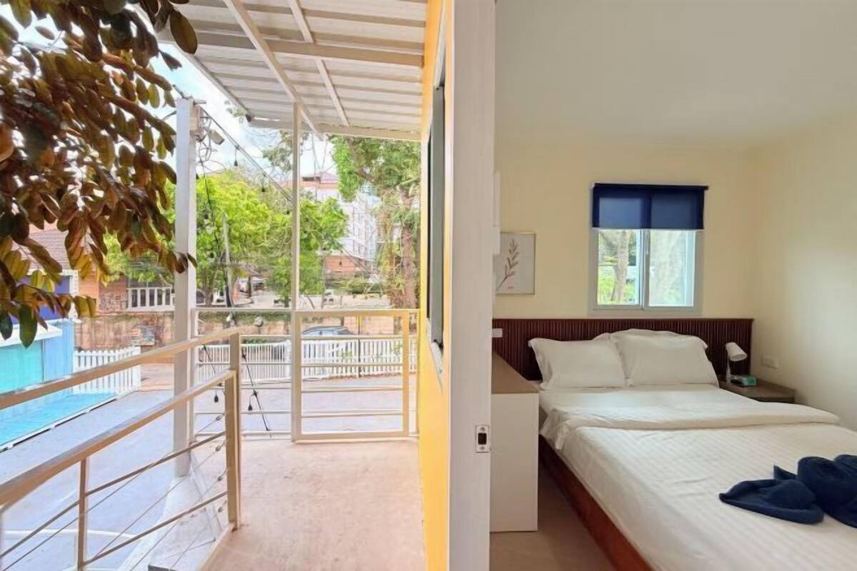 A hotel room with a bed, a nightstand, a window with a blue blind, and a view of the outside.