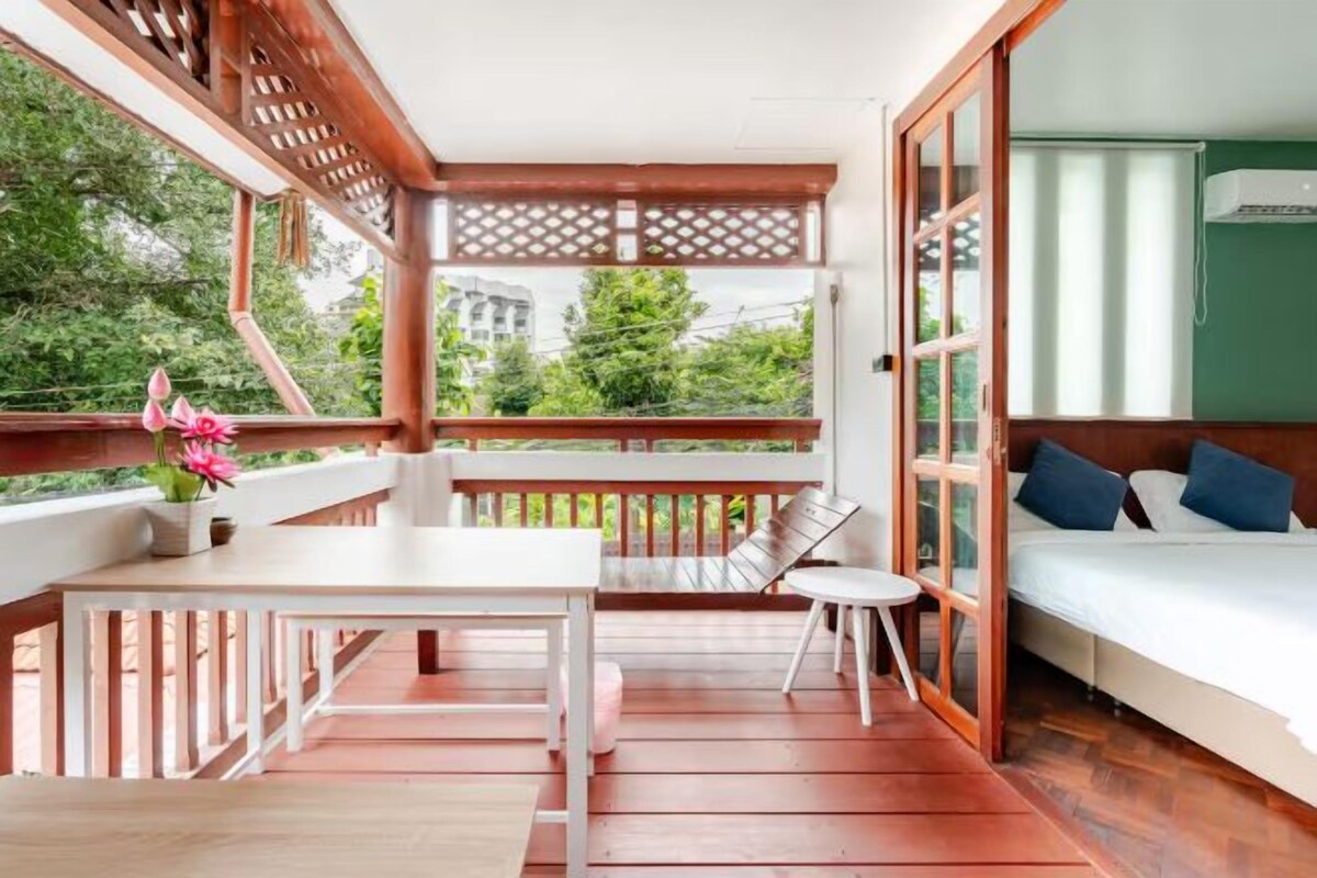 Une pièce avec un lit, une table et un banc. On peut admirer la verdure par la fenêtre.