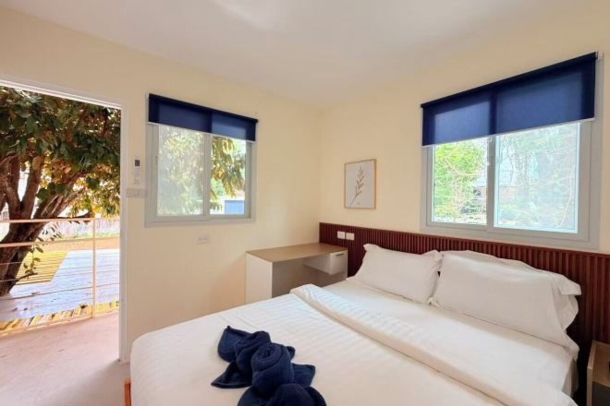 Une chambre d’hôtel avec un lit, un bureau et deux fenêtres équipées de stores.