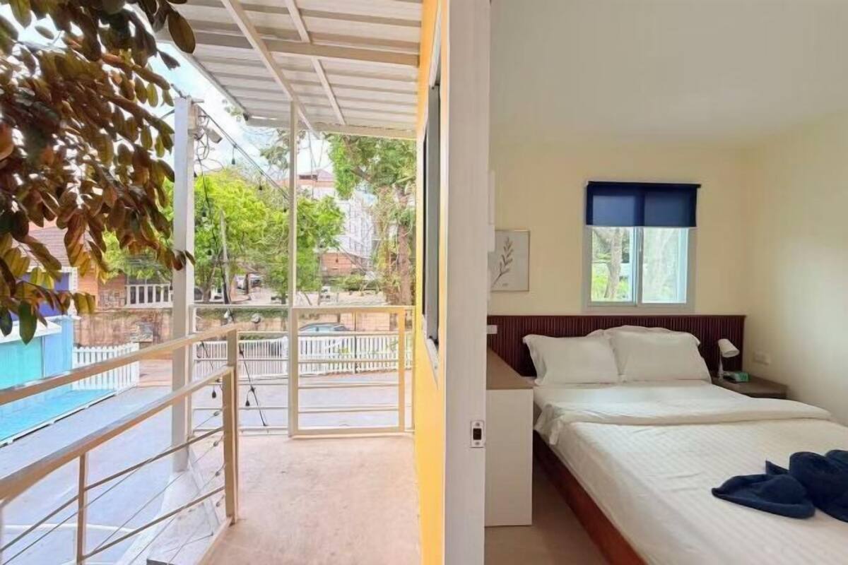 A hotel room with a bed, a nightstand, a window with a blue blind, and a view of the street and buildings outside.