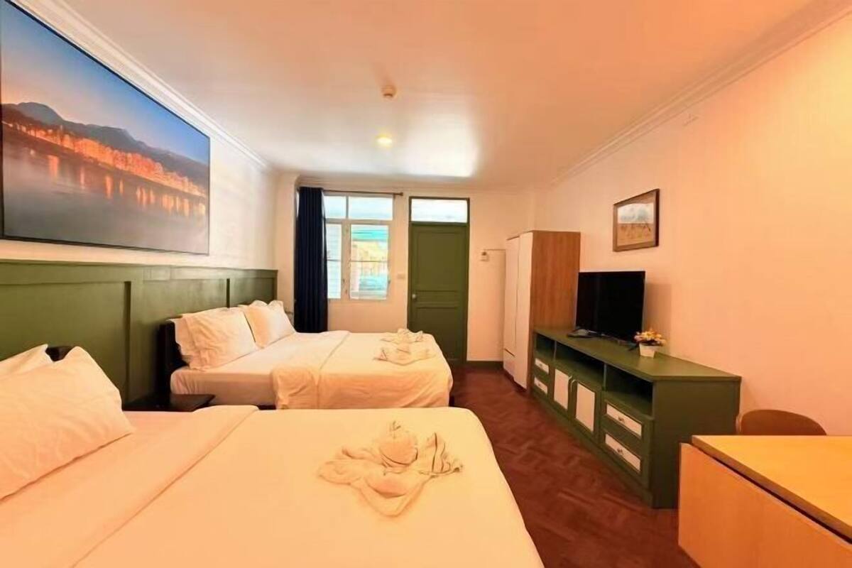 A hotel room with two beds, a television, a desk, and a green cabinet.