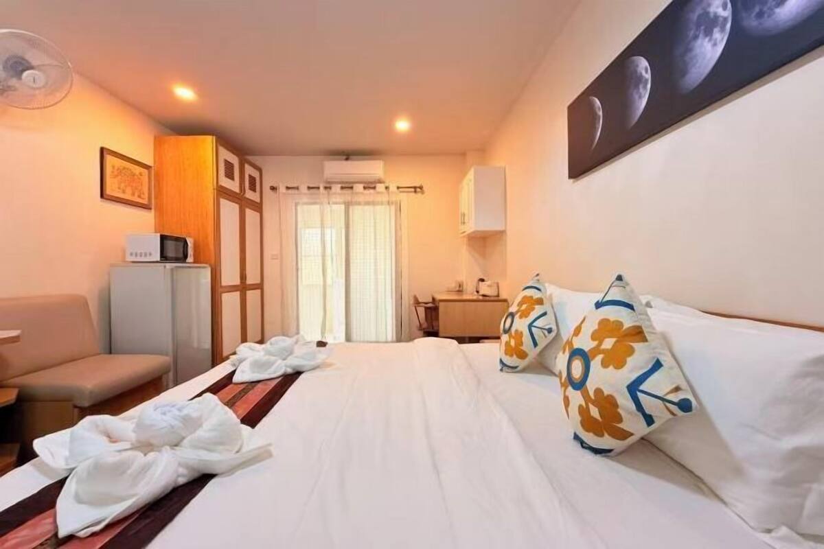 A hotel room with a bed, a desk, a chair, a microwave, and a fan.