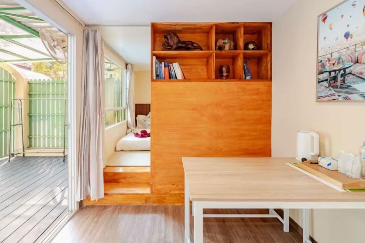 Una habitación con una estantería de madera, una mesa blanca y una ventana con cortinas.