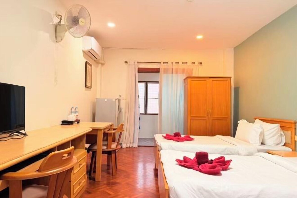 Une chambre d’hôtel avec deux lits, un bureau, une chaise, une télévision et un ventilateur.