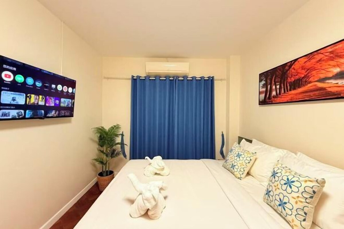 Une chambre d’hôtel avec un lit, un téléviseur fixé au mur, un tableau accroché au mur et un rideau.