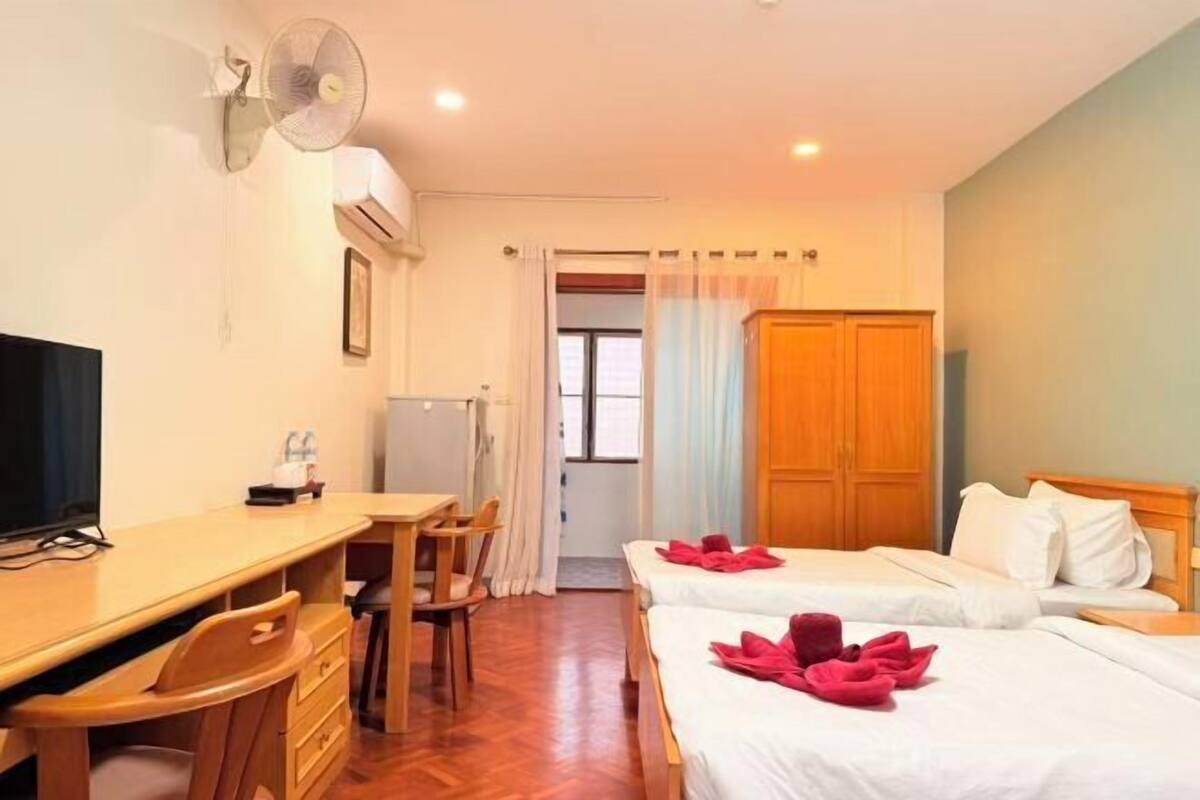 A hotel room with two beds, a desk, a chair, a television, and a fan.